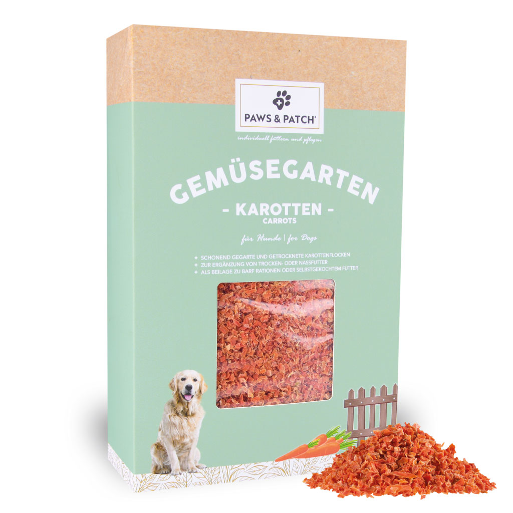 Hellgründe Verpackung aus Pappe mit Sichtfenster, das Karottenflocken zeigt - davor ein Häufchen ausgepackteKarottenflocken